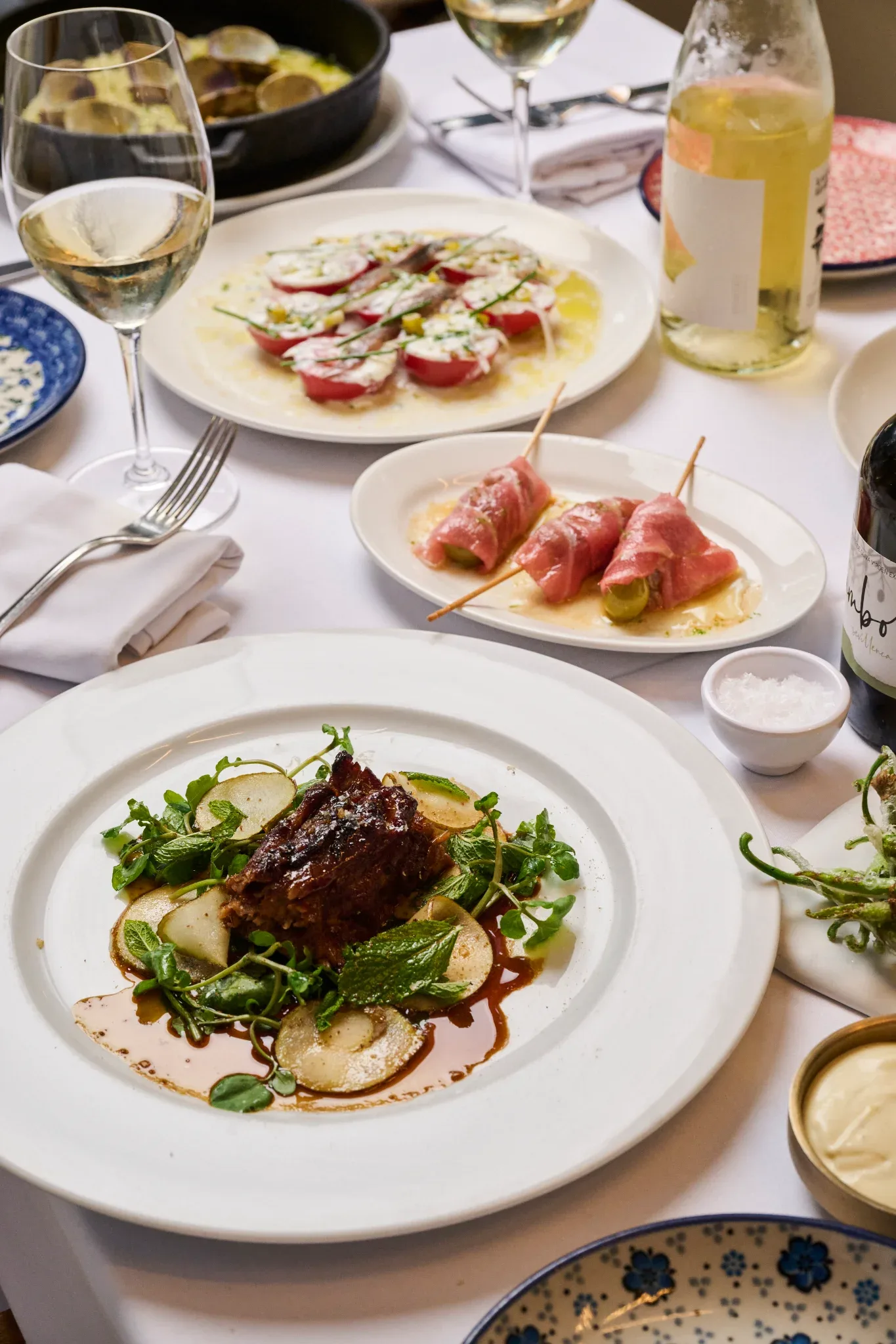 Mesa del Restaurante Igueldo en España con plato principal de carne y guarnición, entrantes fríos y copas de vino blanco
