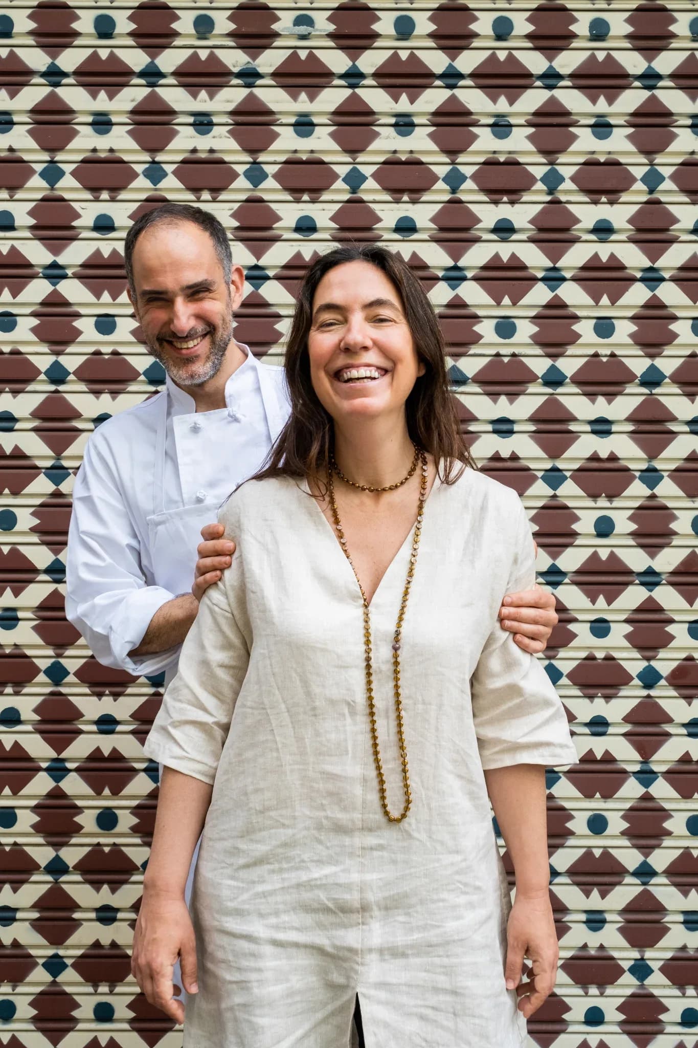 Dos miembros del equipo del Restaurante Igueldo posan sonrientes frente a una persiana decorada en la entrada del local en Barcelona