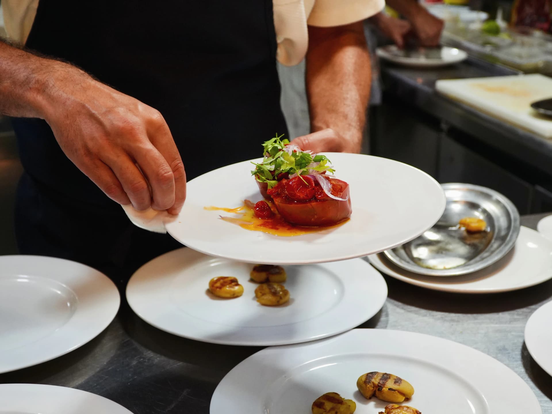 Cocinero emplatando entrante de cocina mediterránea con tomate asado y patatas en Restaurante Igueldo, Barcelona
