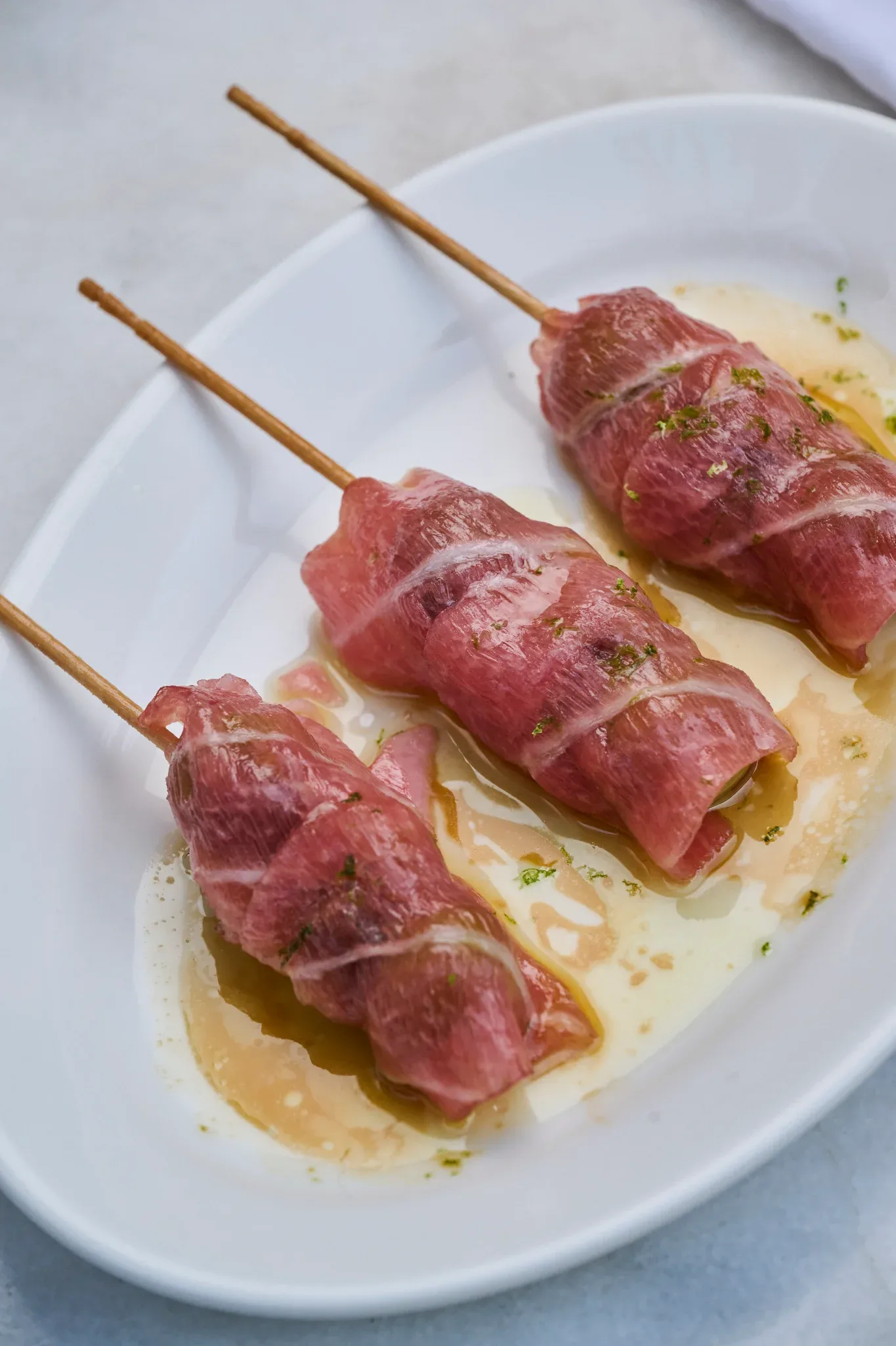 Picaña curada en brochetas sobre plato ovalado con su jugo en Restaurante Igueldo, cocina de tapas en Barcelona