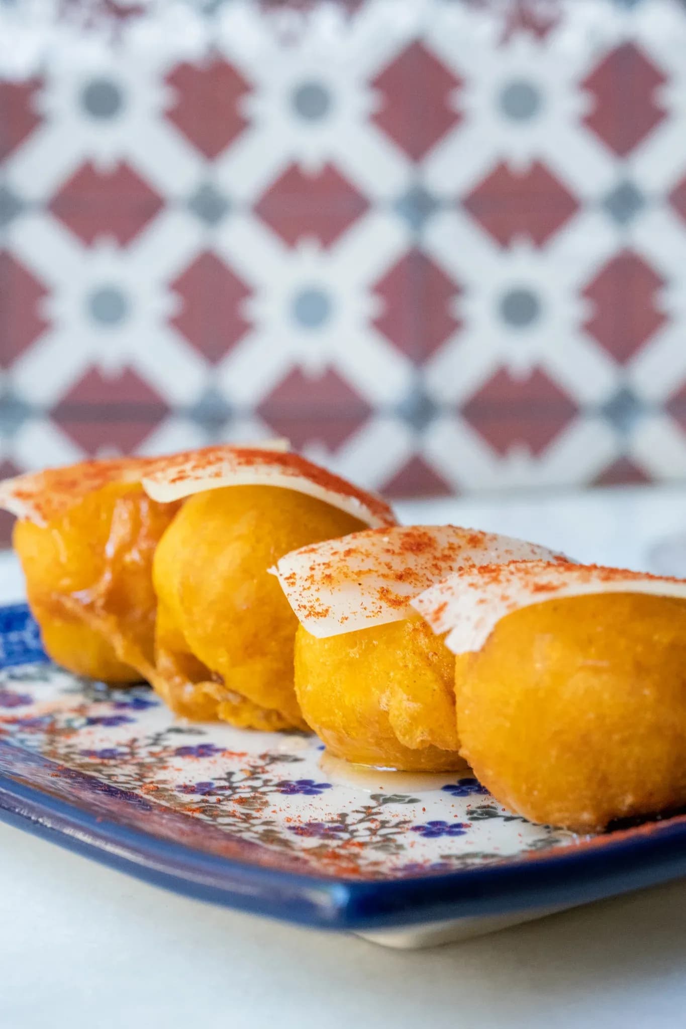 Croqueta del día con láminas de queso y pimentón sobre plato cerámico en Restaurante Igueldo, Barcelona