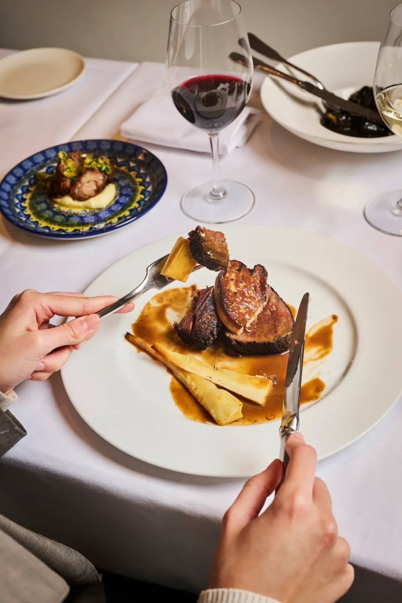 Comensal corta solomillo de vaca con foie gras y salsa de oporto en mesa vestida en Restaurante Igueldo en Barcelona