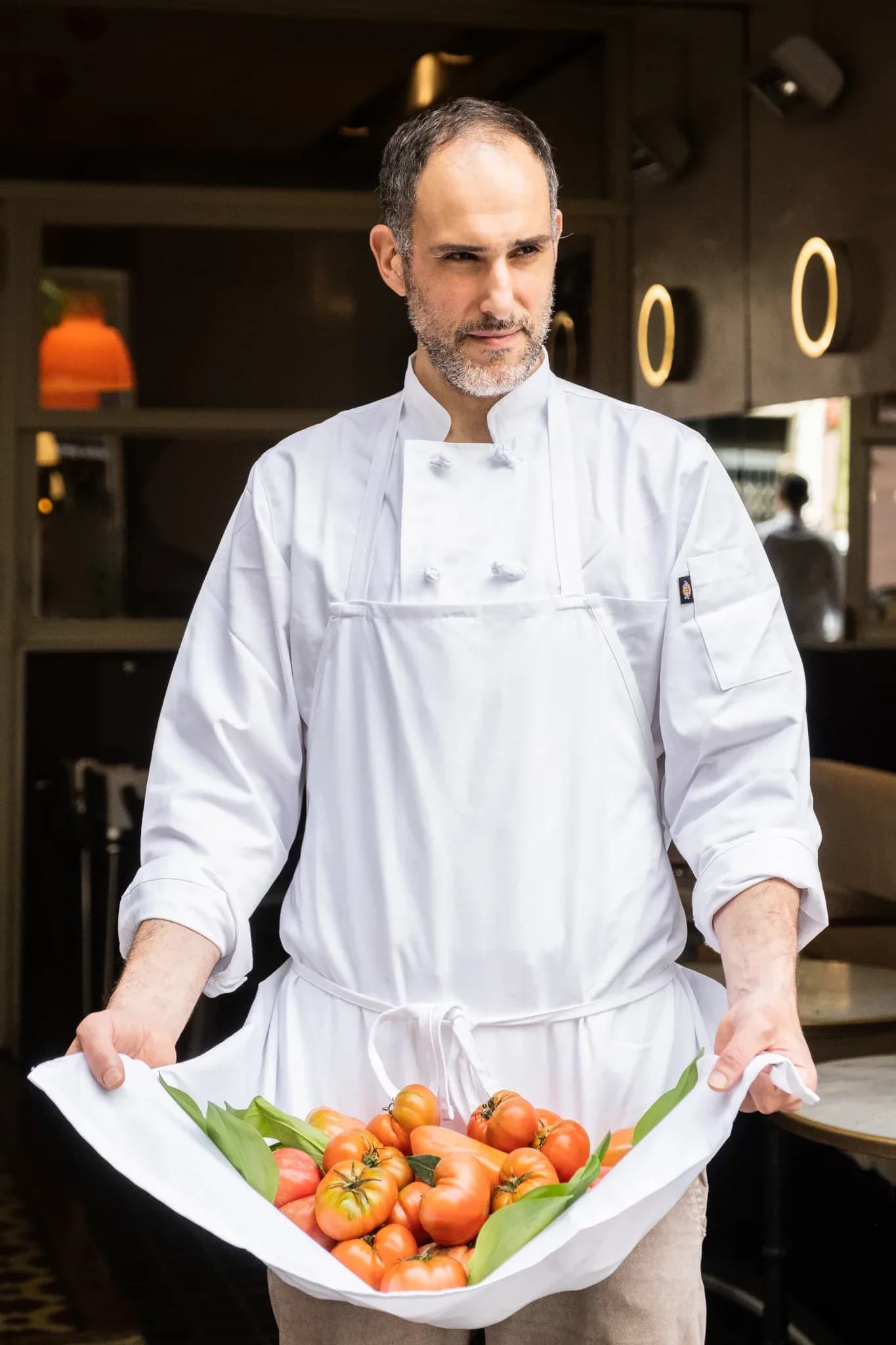 Chef del Restaurante Igueldo en Barcelona sosteniendo un paño blanco lleno de tomates maduros en la entrada del local