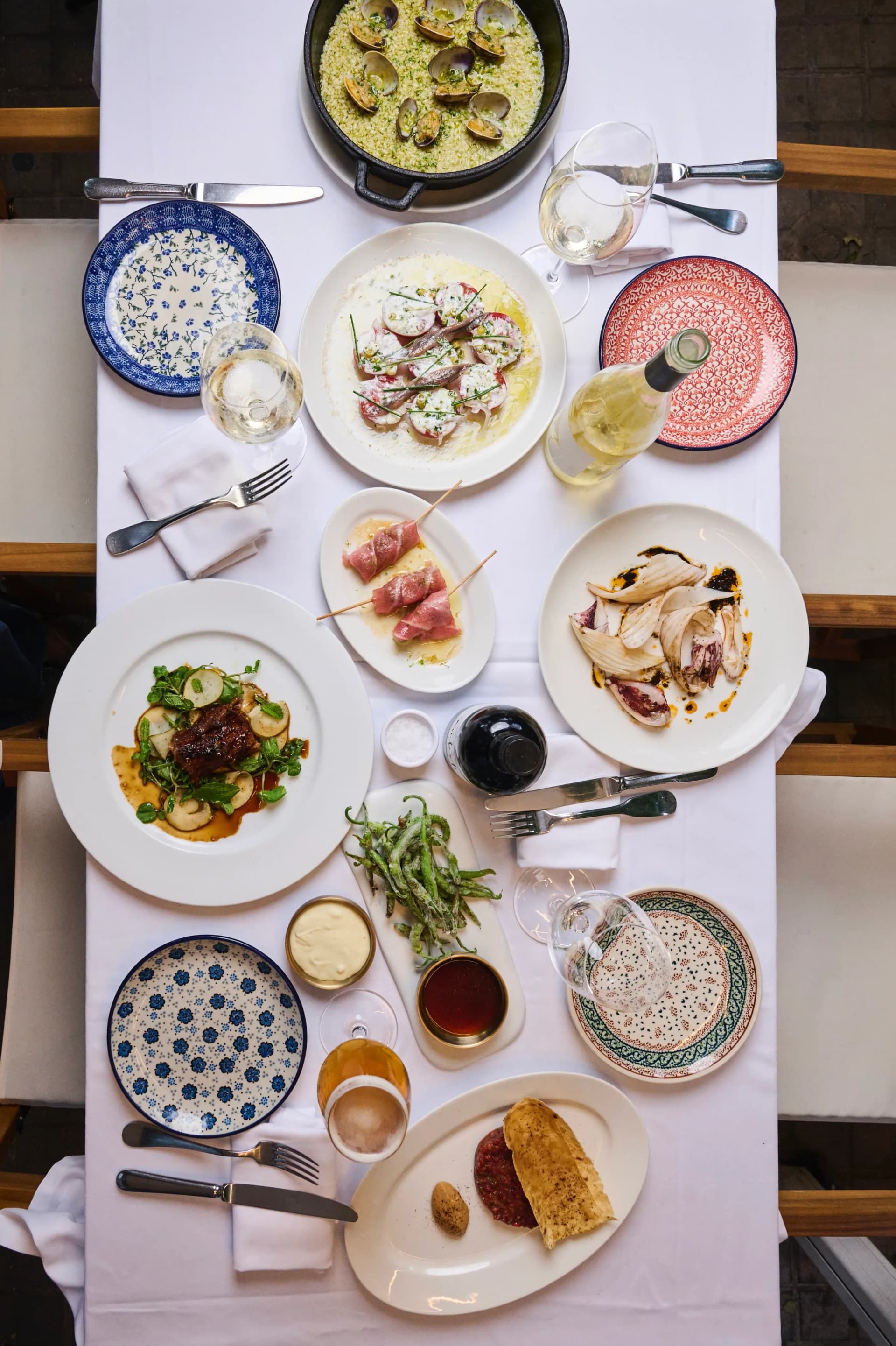 Mesa con varias tapas y platos para compartir, copas de vino blanco y pan en Restaurante Igueldo en Barcelona