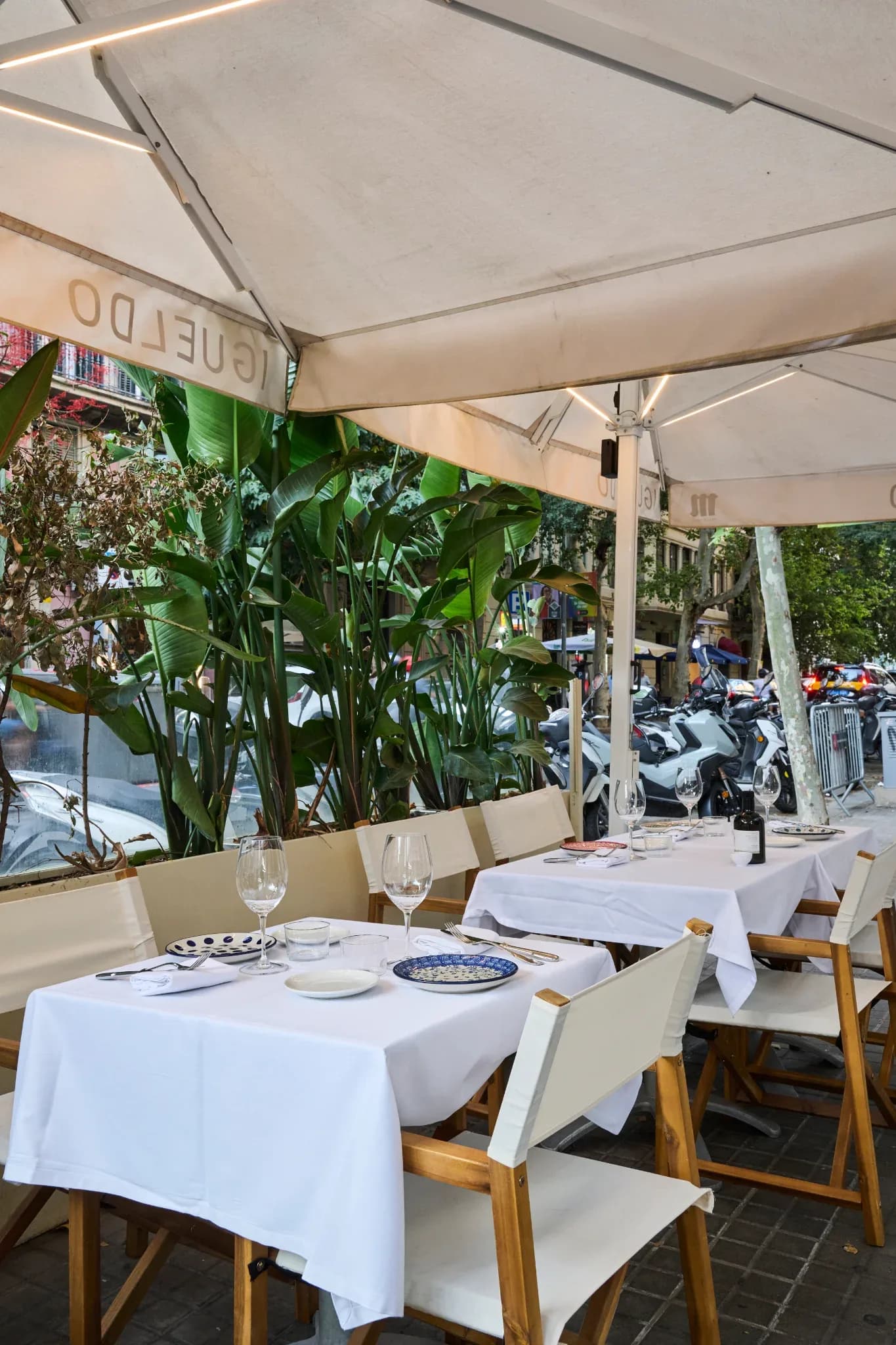 Terraza exterior del Restaurante Igueldo en Barcelona, mesas vestidas con manteles blancos y copas junto a plantas y la calle