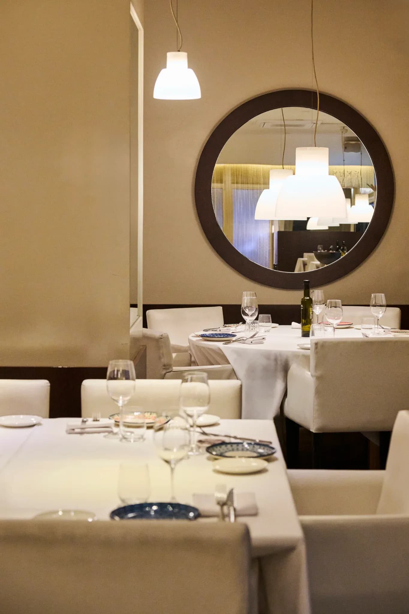 Salón interior del Restaurante Igueldo en Barcelona, mesas vestidas de blanco, copas de vino y gran espejo redondo en la pared