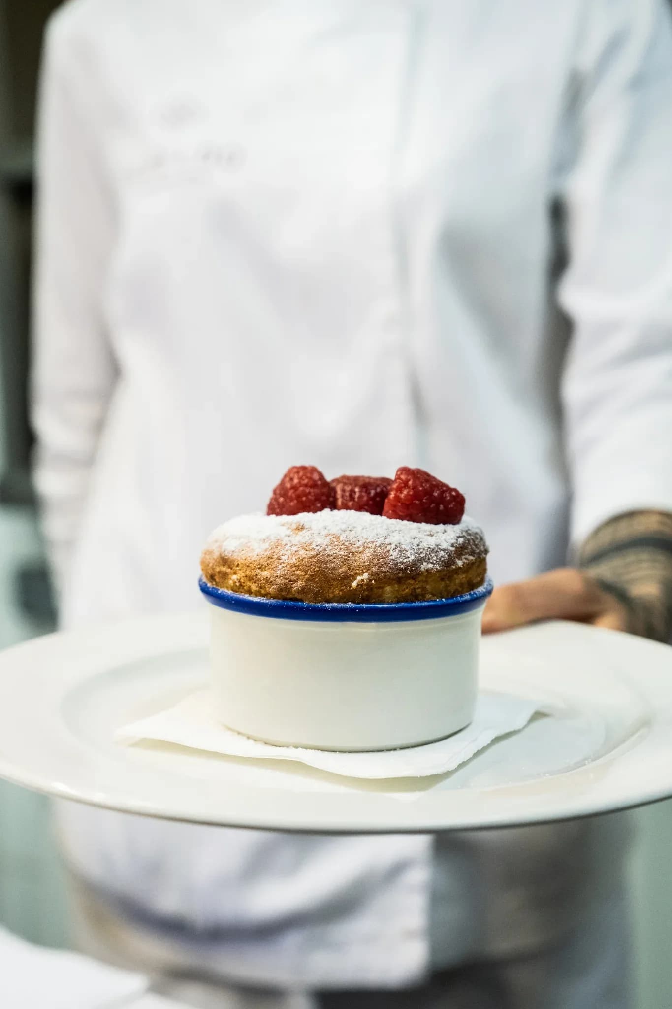 Soufflé individual espolvoreado con azúcar glas y frambuesas frescas sobre plato blanco en Restaurante Igueldo, Barcelona