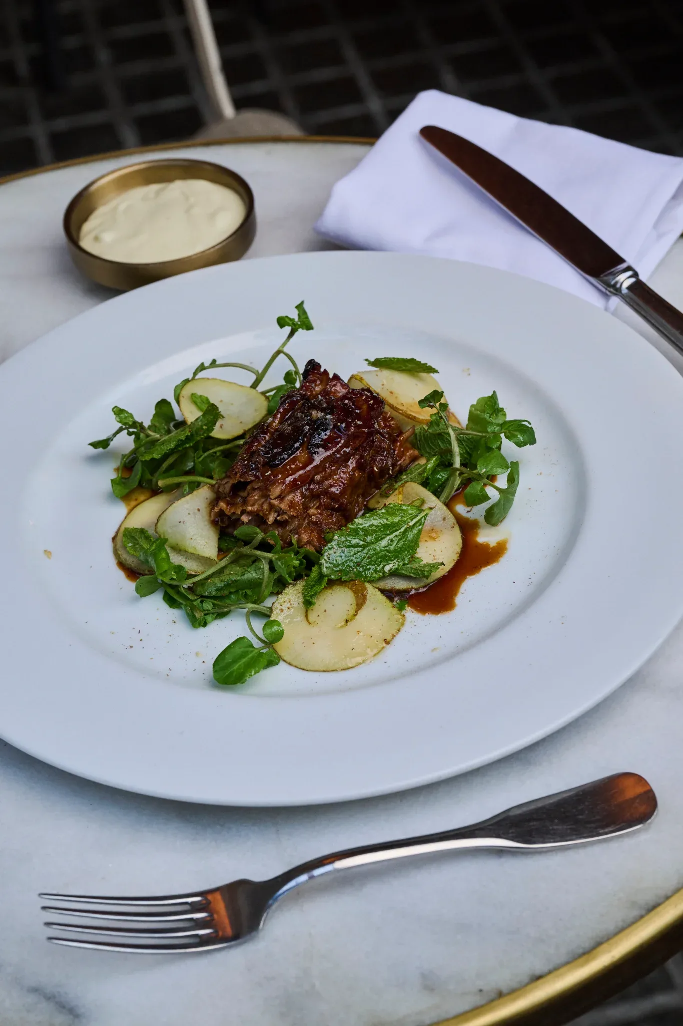 Plato de carne glaseada sobre ensalada templada de hojas verdes y láminas de patata en Restaurante Igueldo, Barcelona